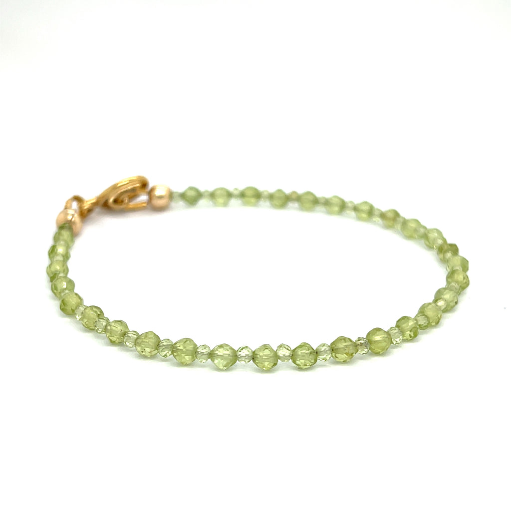 A peridot gemstone 2-3mm faceted round with a gold filled toggle on a white background front overview.