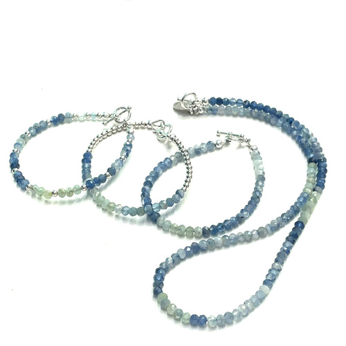 A photograph of three beaded gemstone bracelets with a matching necklace, one with blue and green kyanite beads and another with a similar color scheme, both featuring sterling silver toggle clasps. On a white background, front overview. 