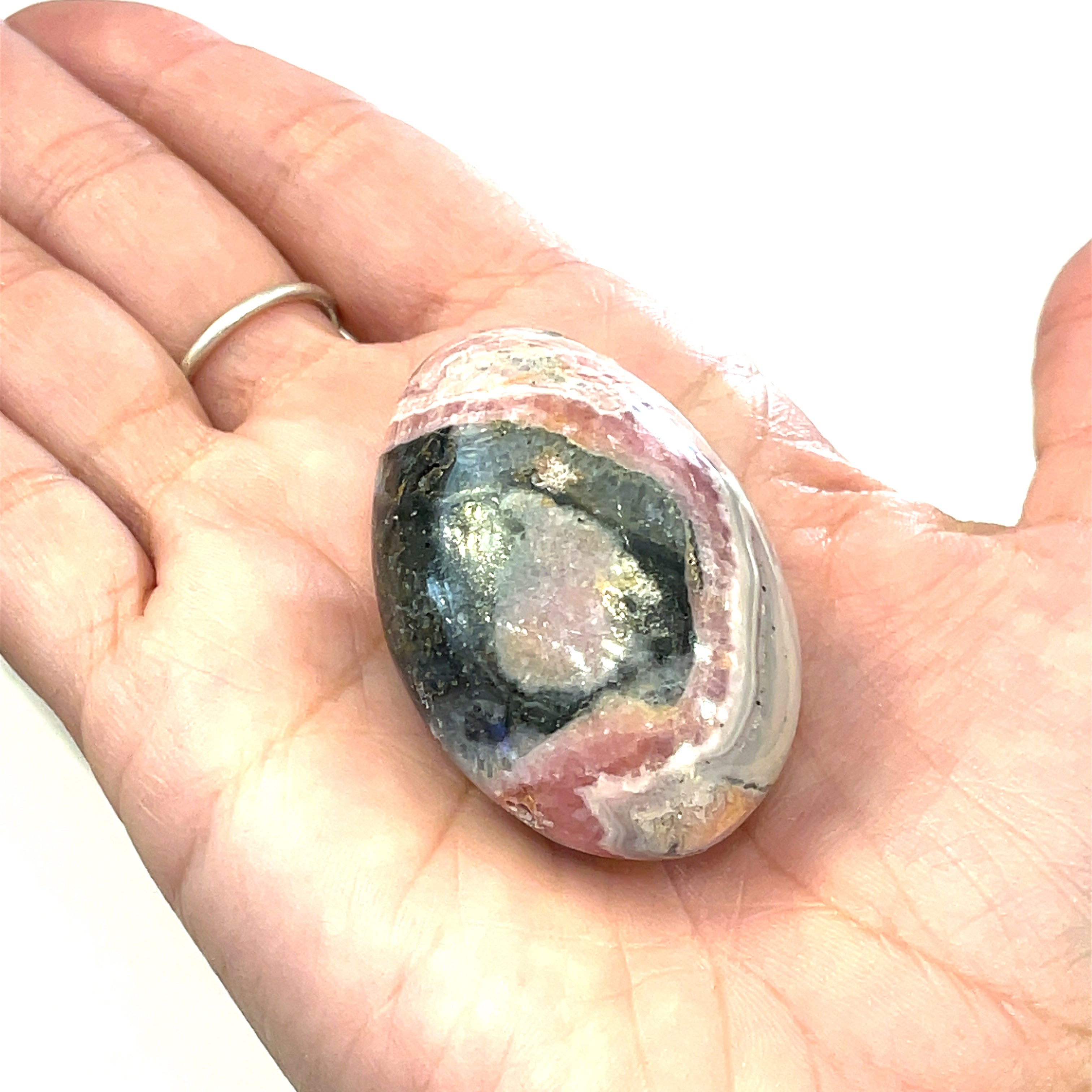 A polished Rhodochrosite gemstone palm stones with varying shades of pink to pale brown colors and white streaks on a white background front overview in a models hand. 