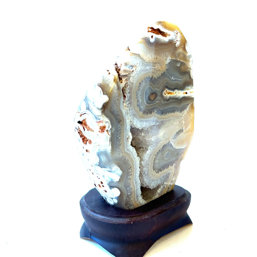 A polished agate geode gemstone collector piece is displayed on a wooden stand, showcasing its intricate patterns and colors on a white background, right angled view