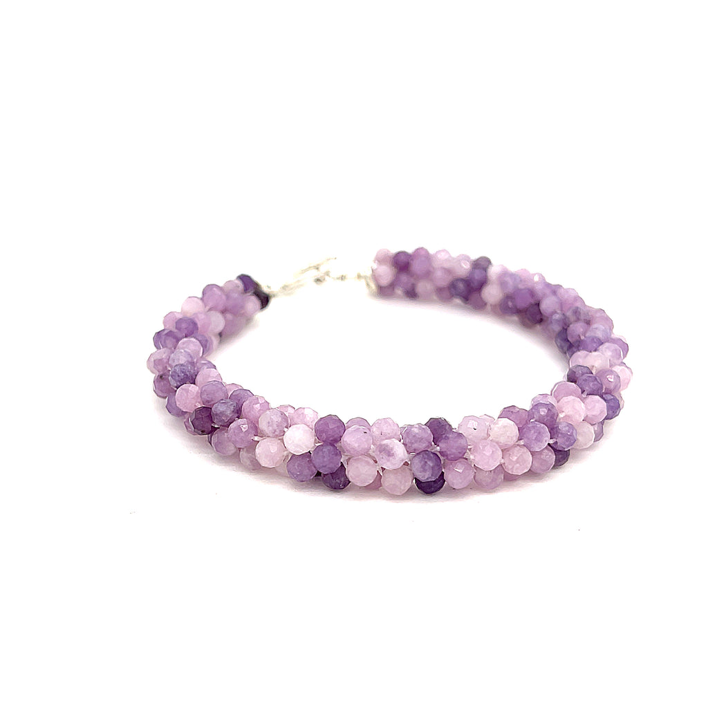 A purple sugilite gemstone bracelet with a sterling silver simple circle toggle, crocheted into a tubular pattern on a white background, front overview. 