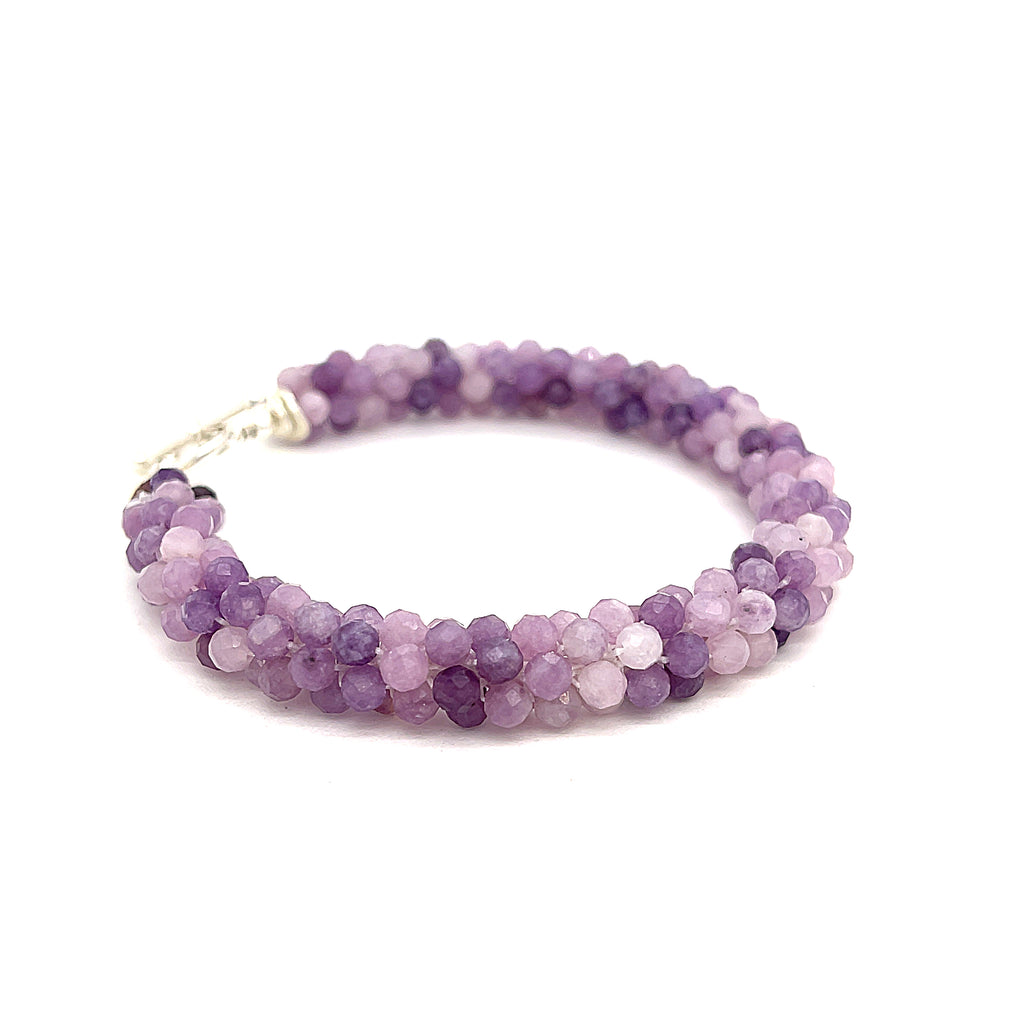 A purple sugilite gemstone bracelet with a sterling silver simple circle toggle, crocheted into a tubular pattern on a white background, front right angle overview. 