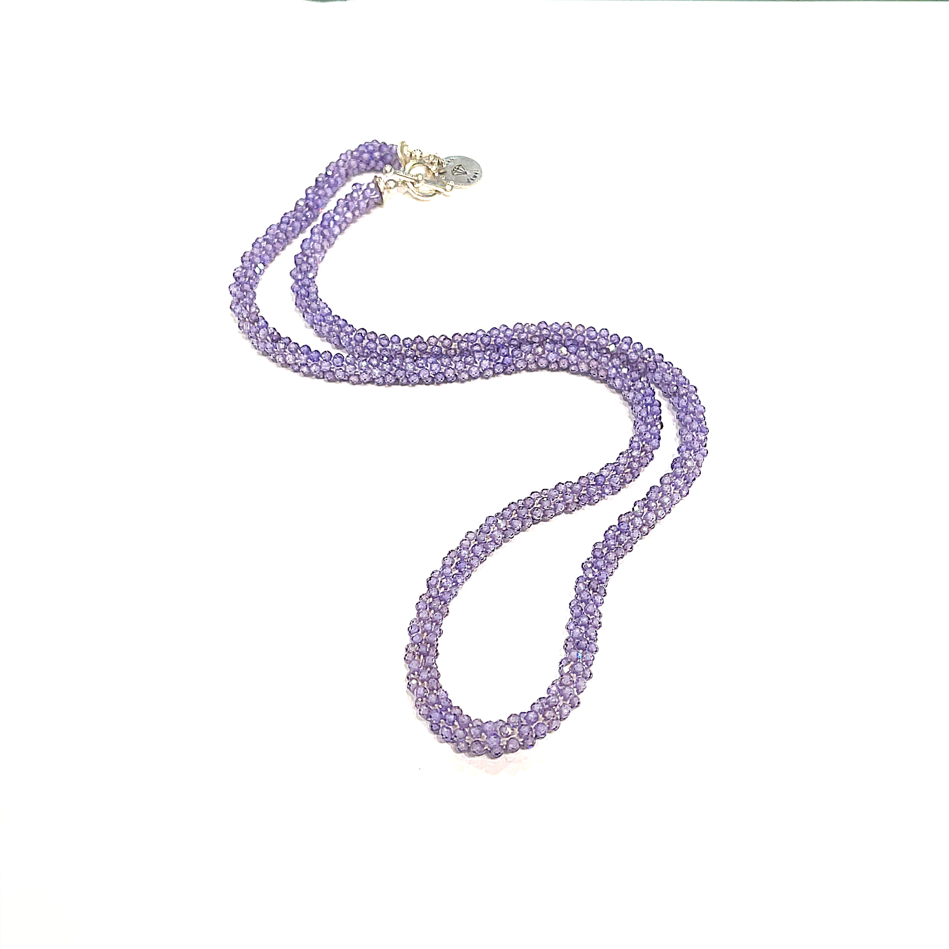 A purple zircon gemstone crocheted necklace with a sterling silver toggle, on a white background. A long, center, close-up overview. 