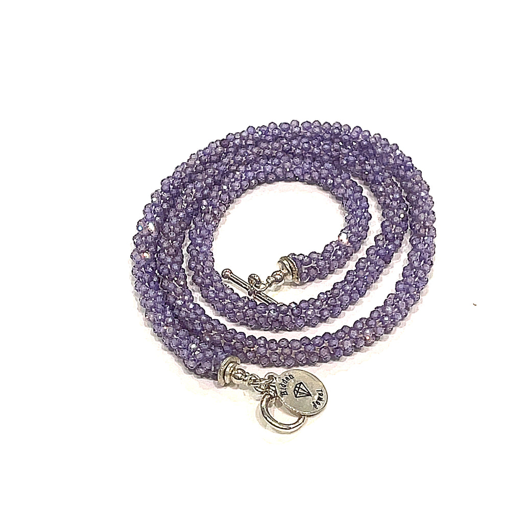 A purple zircon gemstone crocheted necklace with a sterling silver toggle, on a white background. A spiral overview. 