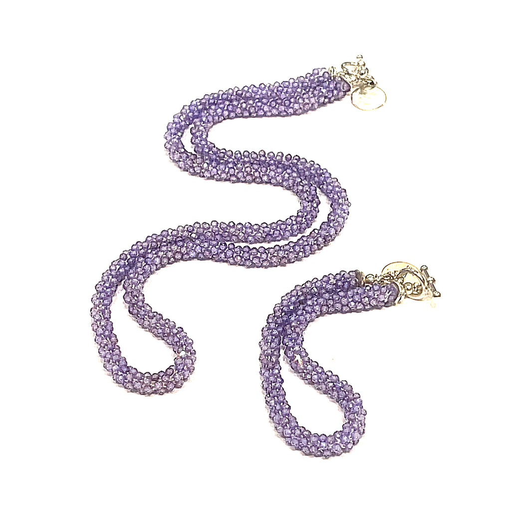 A purple zircon gemstone crocheted necklace with a sterling silver toggle, on a white background with its matching bracelet. A long front diagonal overview. 
