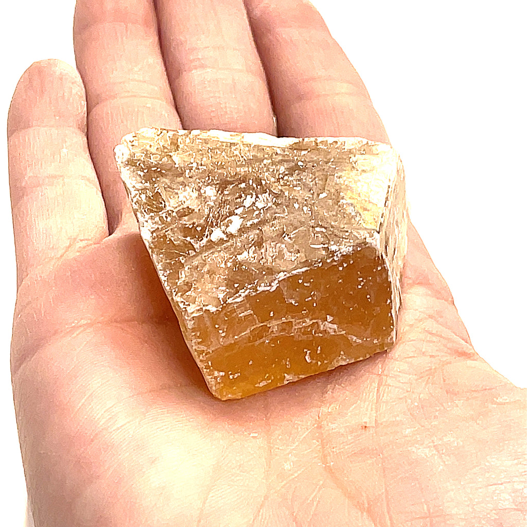 A raw honey calcite gemstones displayed in a models palm on a white background, front view.