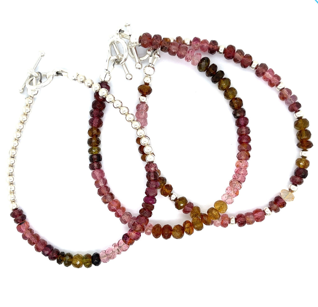 A series of beaded bracelets featuring tourmaline gemstones in various shades of pink, brown, and green, with sterling silver accents and a silver toggle on a white background, front and center overview.