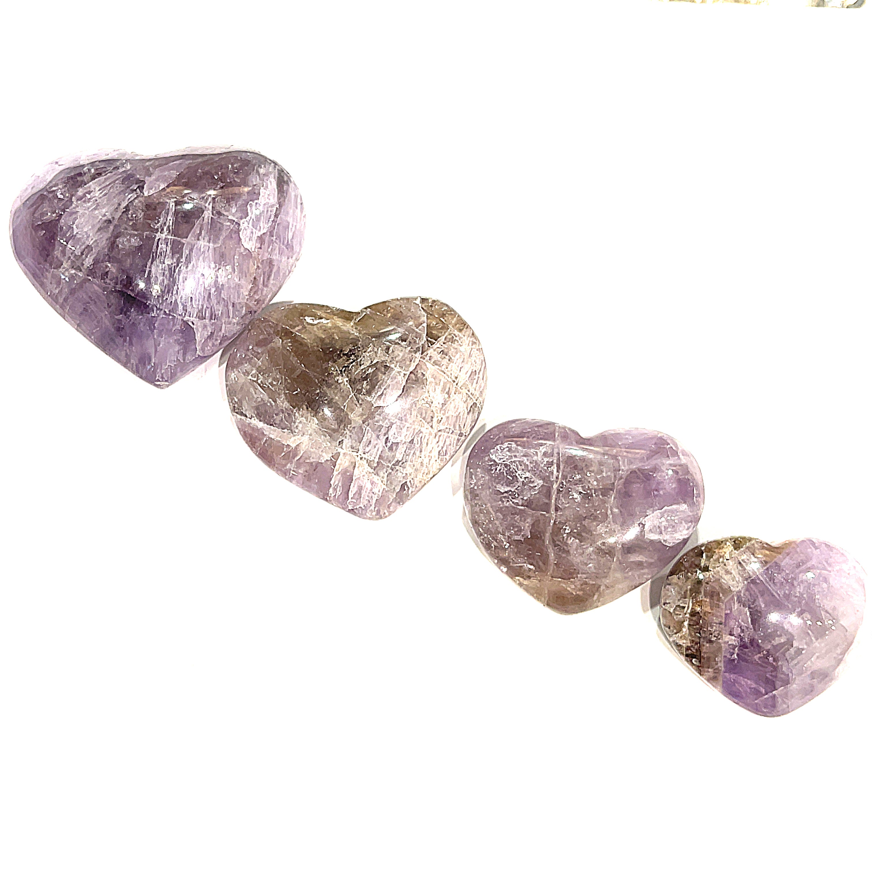 A series of heart-shaped Super Seven gemstone carvings, with varying shades of purple and brown, arranged in a line on a white background, front overview. 