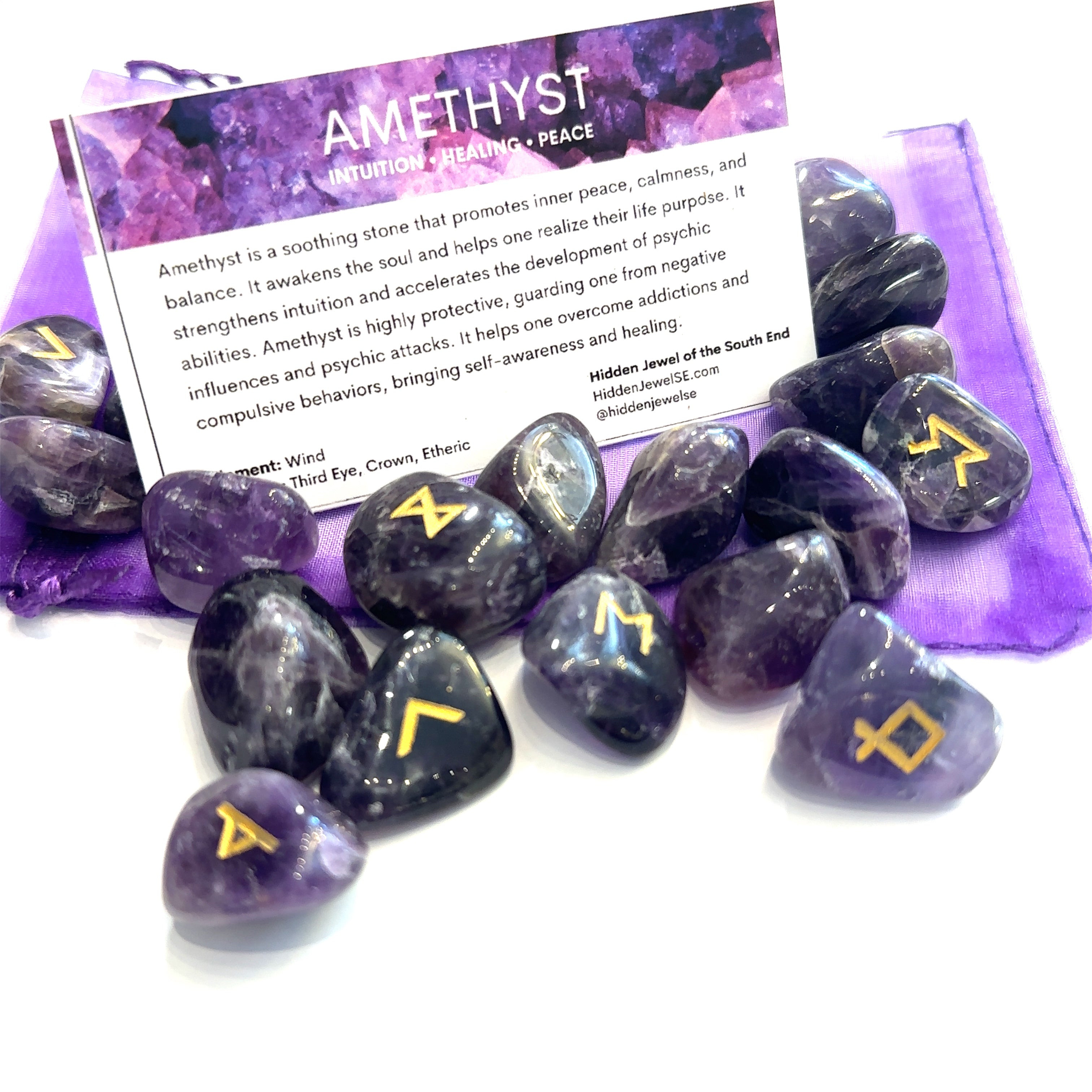 A set of gemstone runes inscribed with symbols, displayed alongside a purple fabric and information cards, against a white background, front view