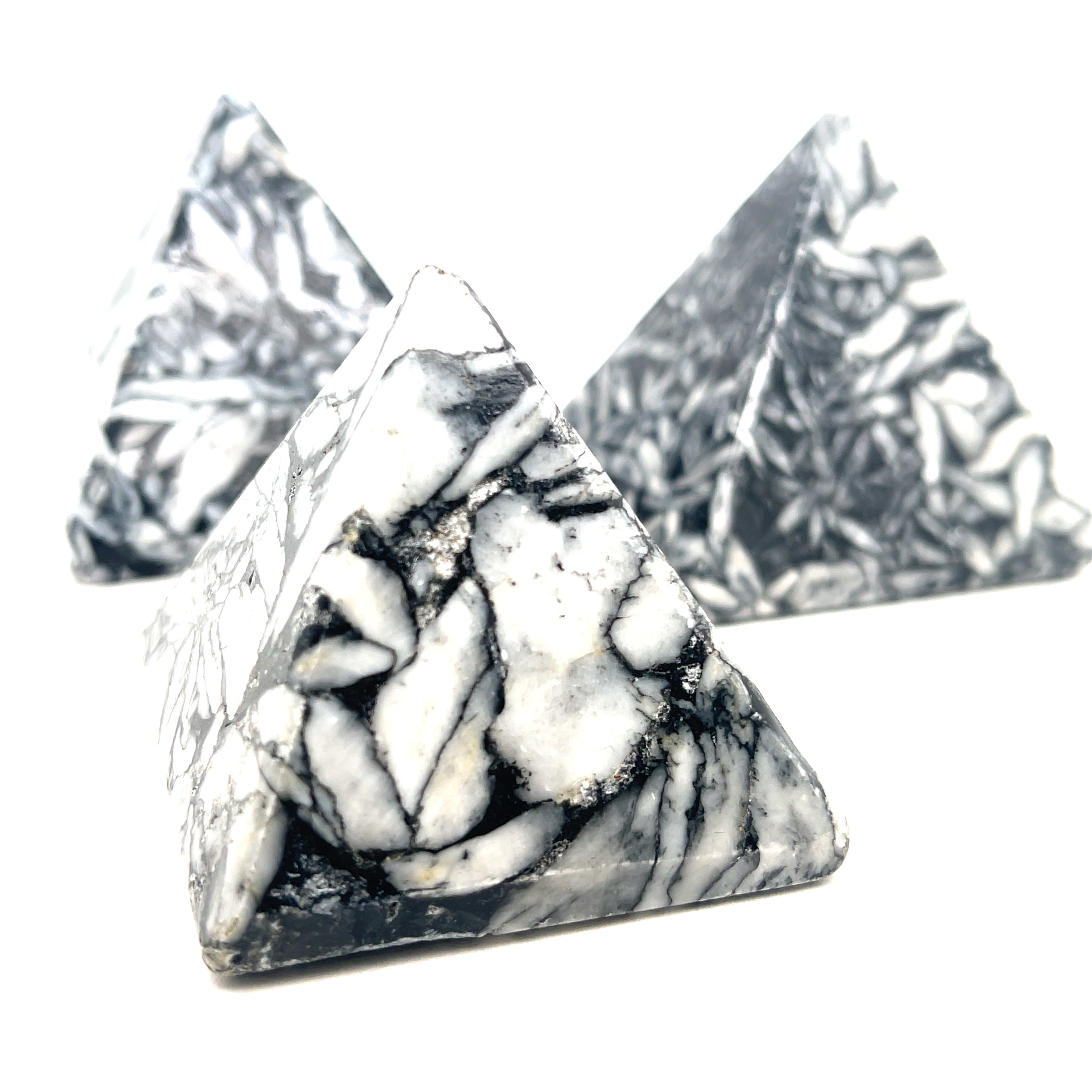 A set of three Pinolith gemstone pyramids with a mottled black and white appearance, displayed on a white background, front overview.