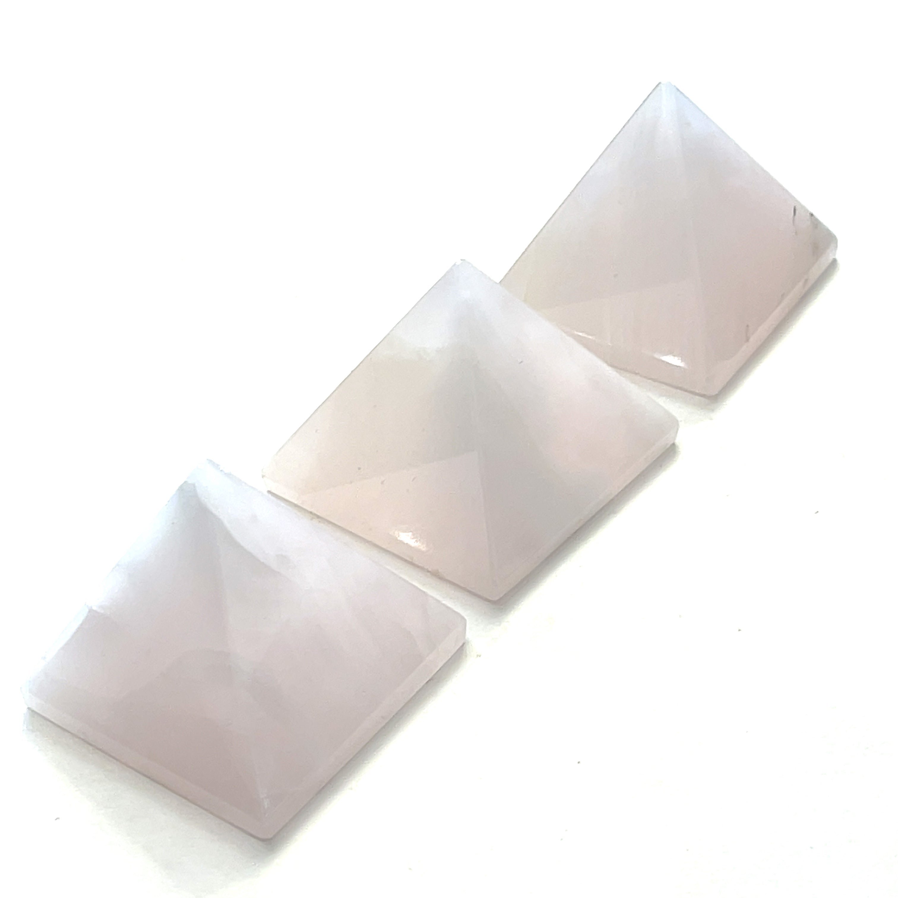 A set of three pink Mangano Calcite pyramid-shaped gemstones displayed on a white background. On a white background, center overview. 