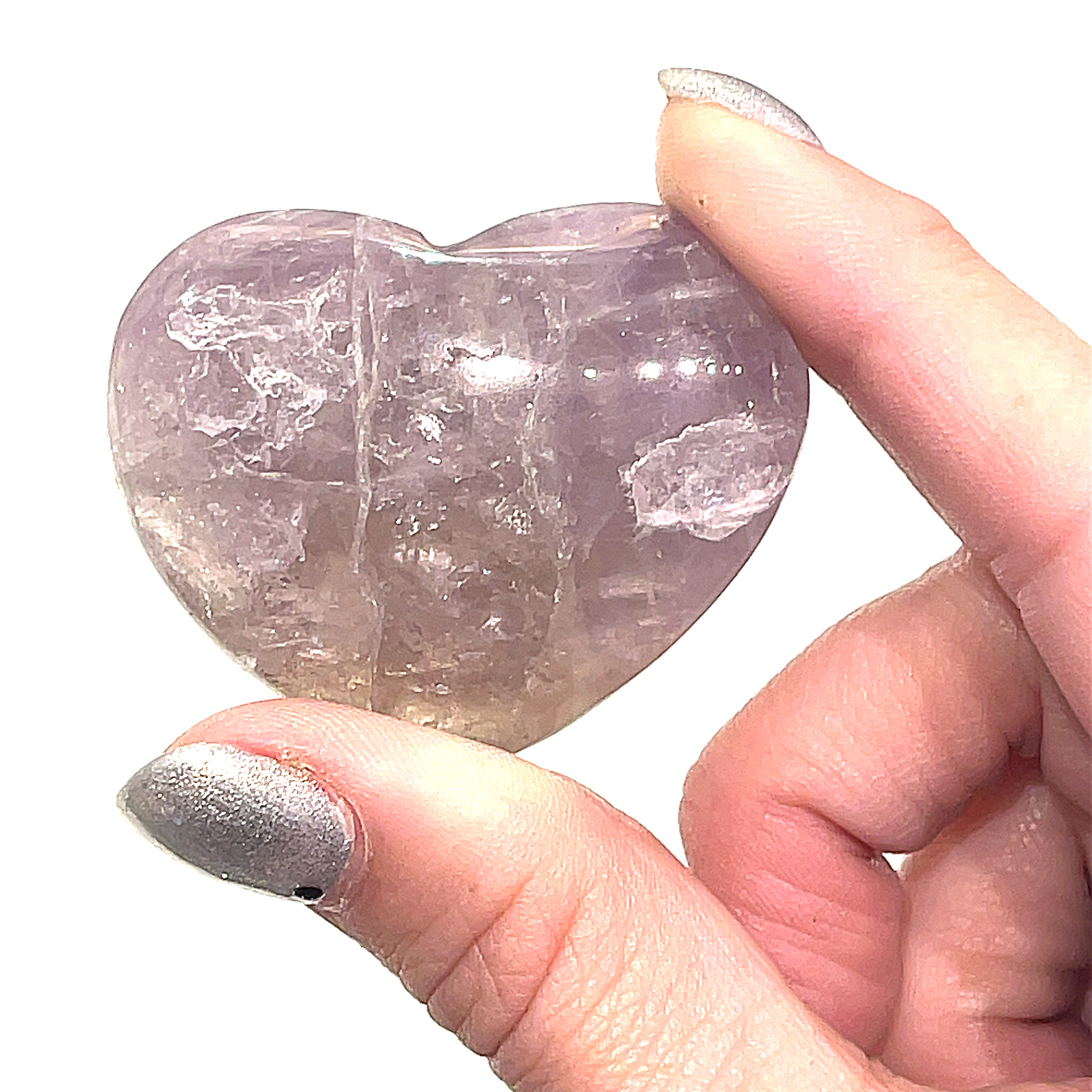 A small Super Seven gemstone heart carving, held by a model for a close-up, front view on a white background.
