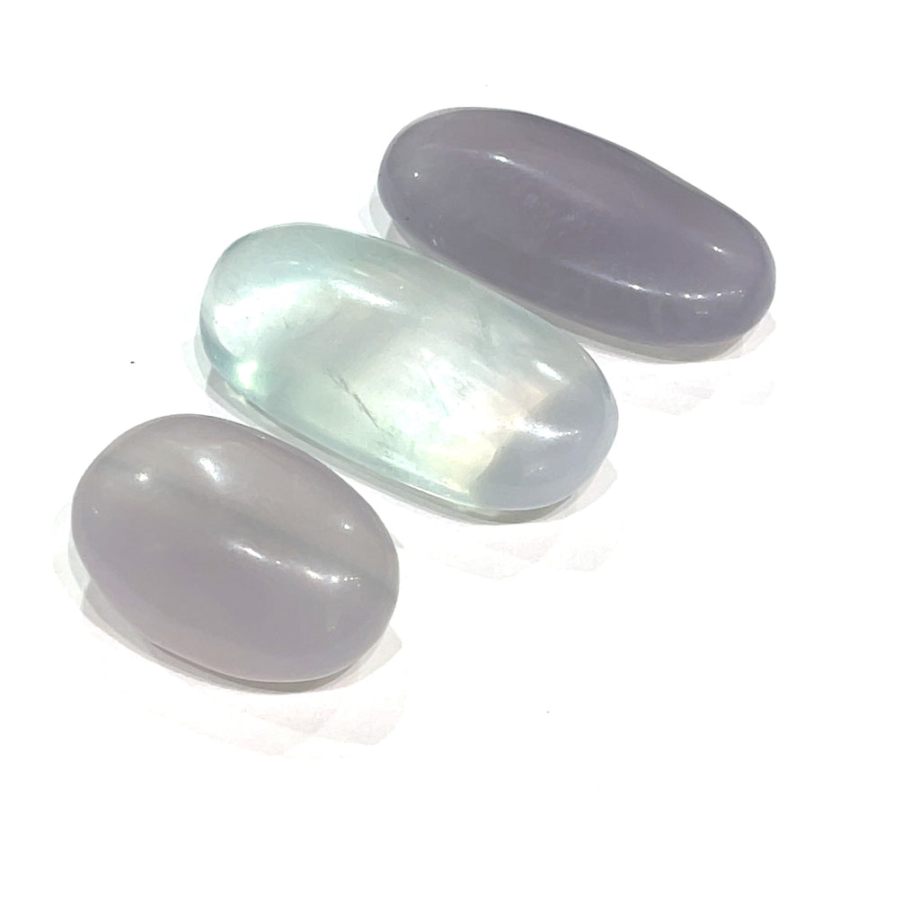 A smaller grouping of smooth, rounded gemstone palm stones displaying varying shades of lavender and green, with a milky translucency on a white background close up  overview.