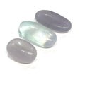 A smaller grouping of smooth, rounded gemstone palm stones displaying varying shades of lavender and green, with a milky translucency on a white background close up  overview.