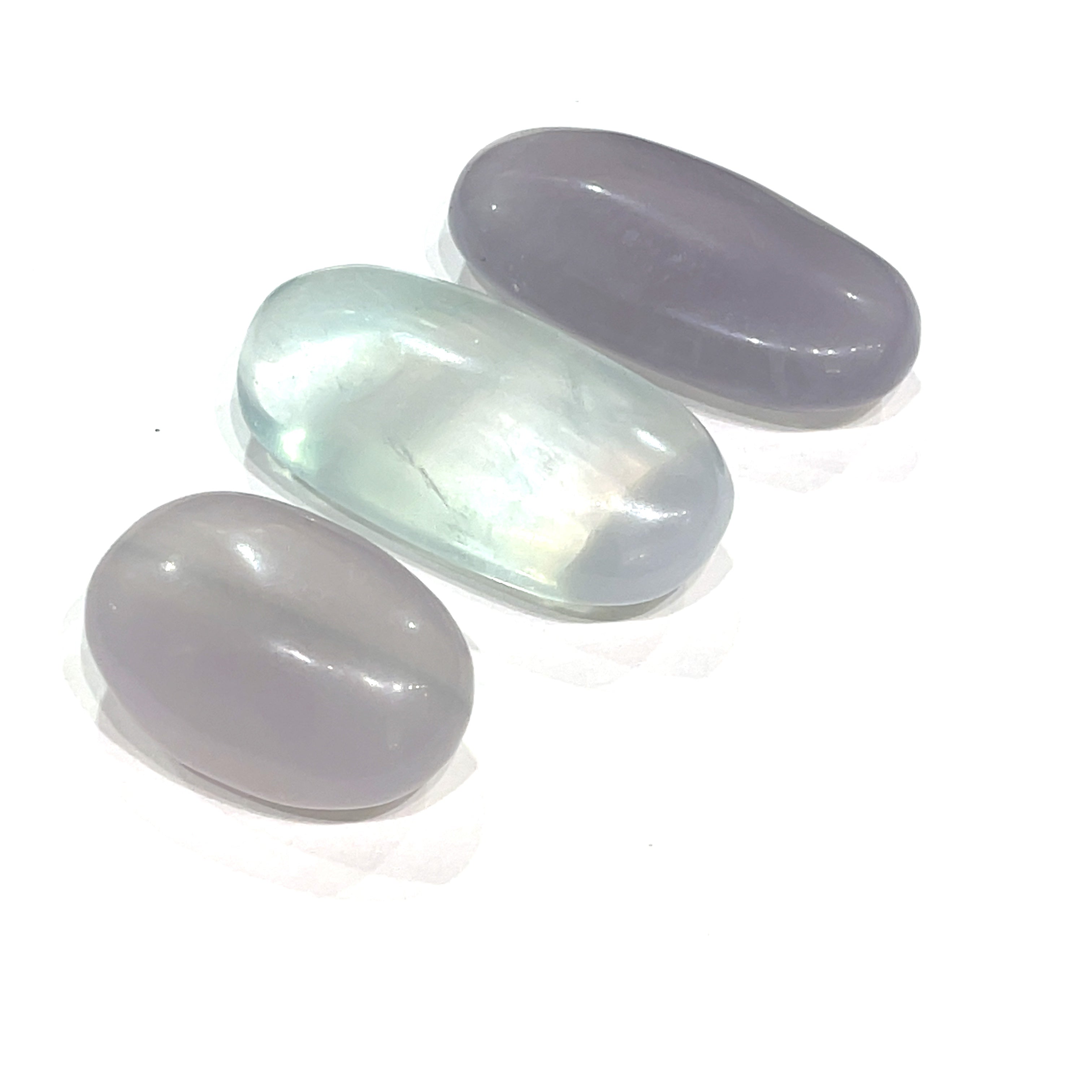 A smaller grouping of smooth, rounded gemstone palm stones displaying varying shades of lavender and green, with a milky translucency on a white background close up  overview.