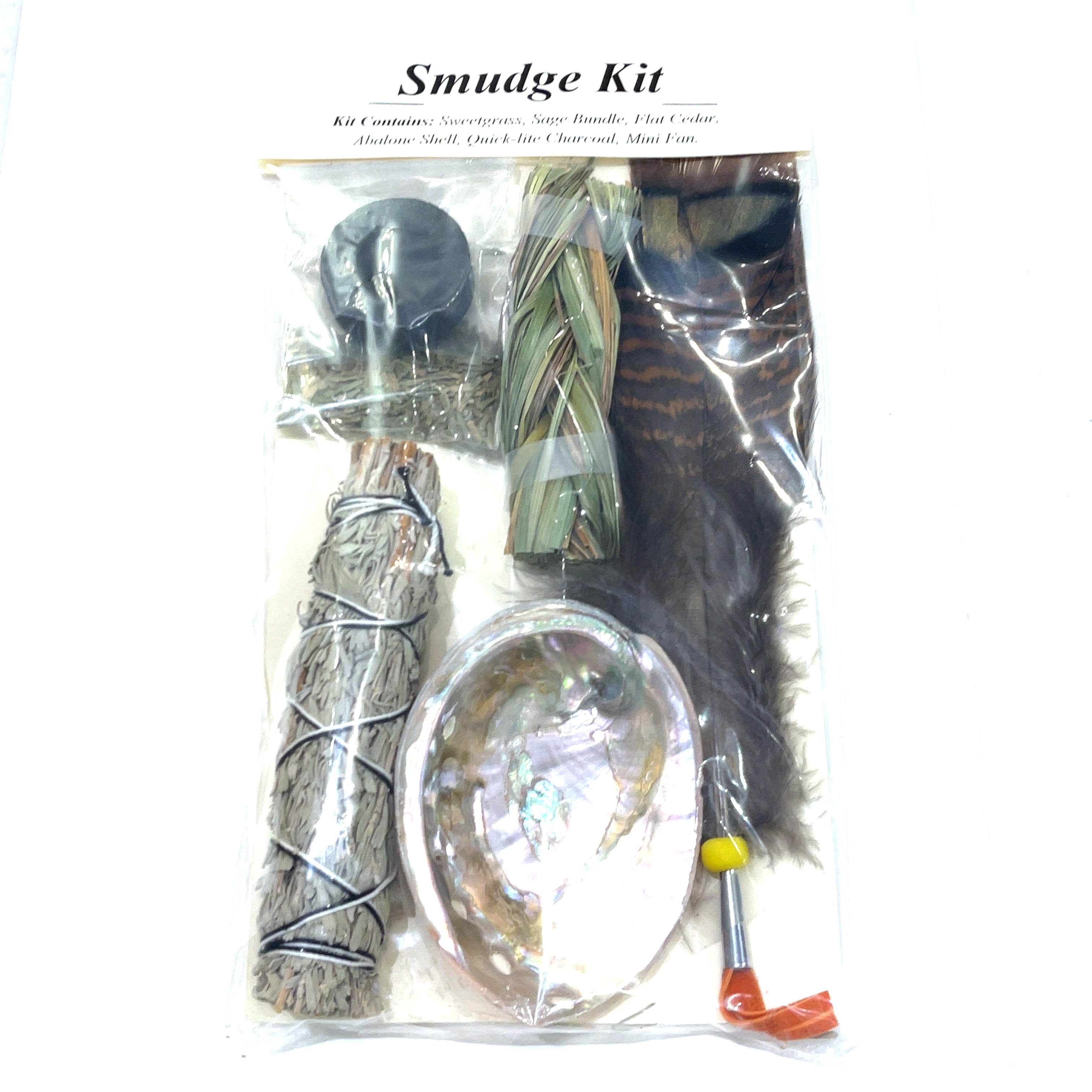 A smudge kit including a bundle of sage, sweetgrass, flat cedar, an abalone shell, quick-lite charcoal, and a mini fan, all packaged in clear plastic on a white background, front view. 