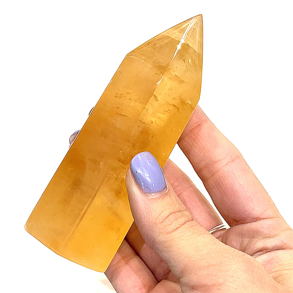 Another Honey Calcite gemstone towers displayed in a models hand on a white background, front view.