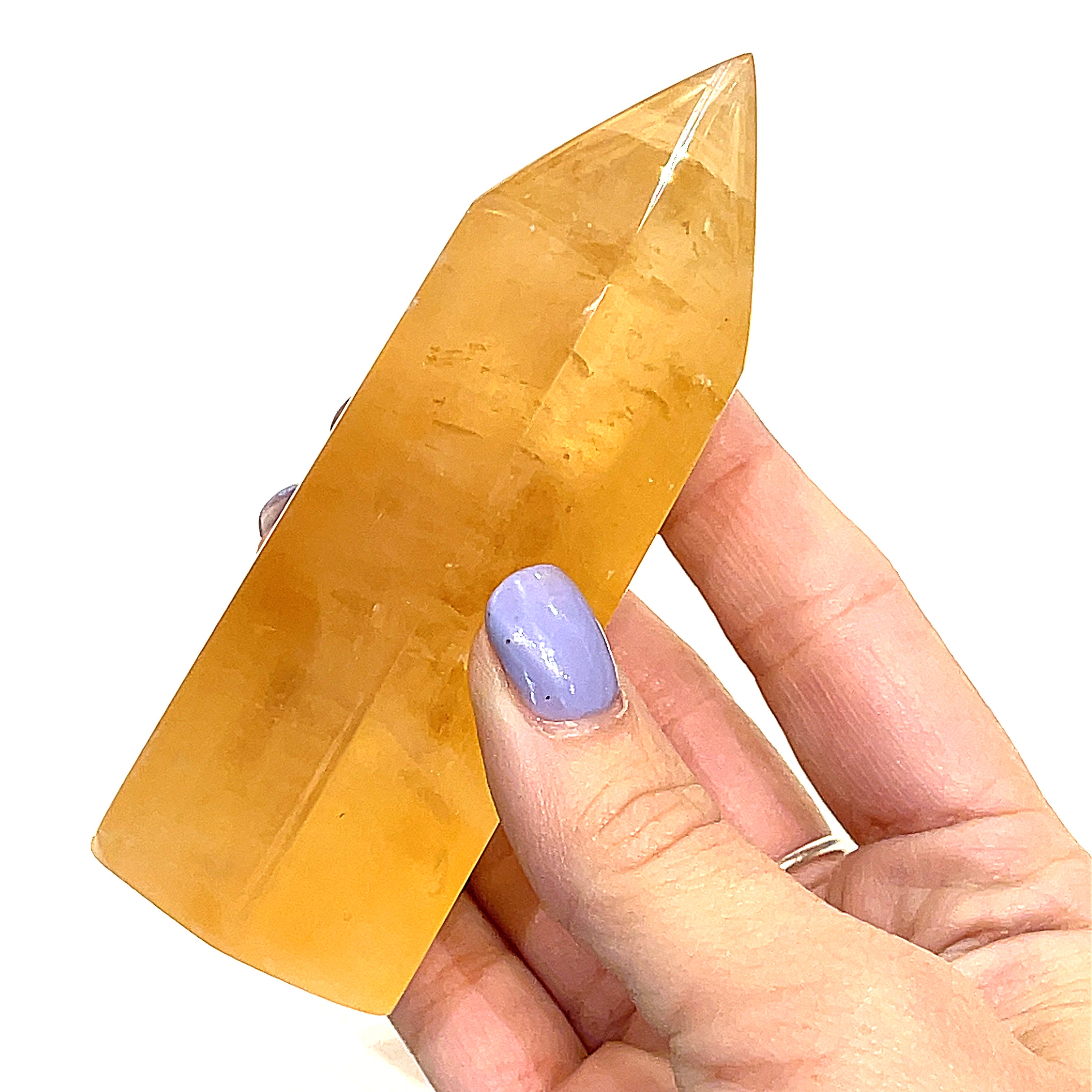 Another Honey Calcite gemstone towers displayed in a models hand on a white background, front view.