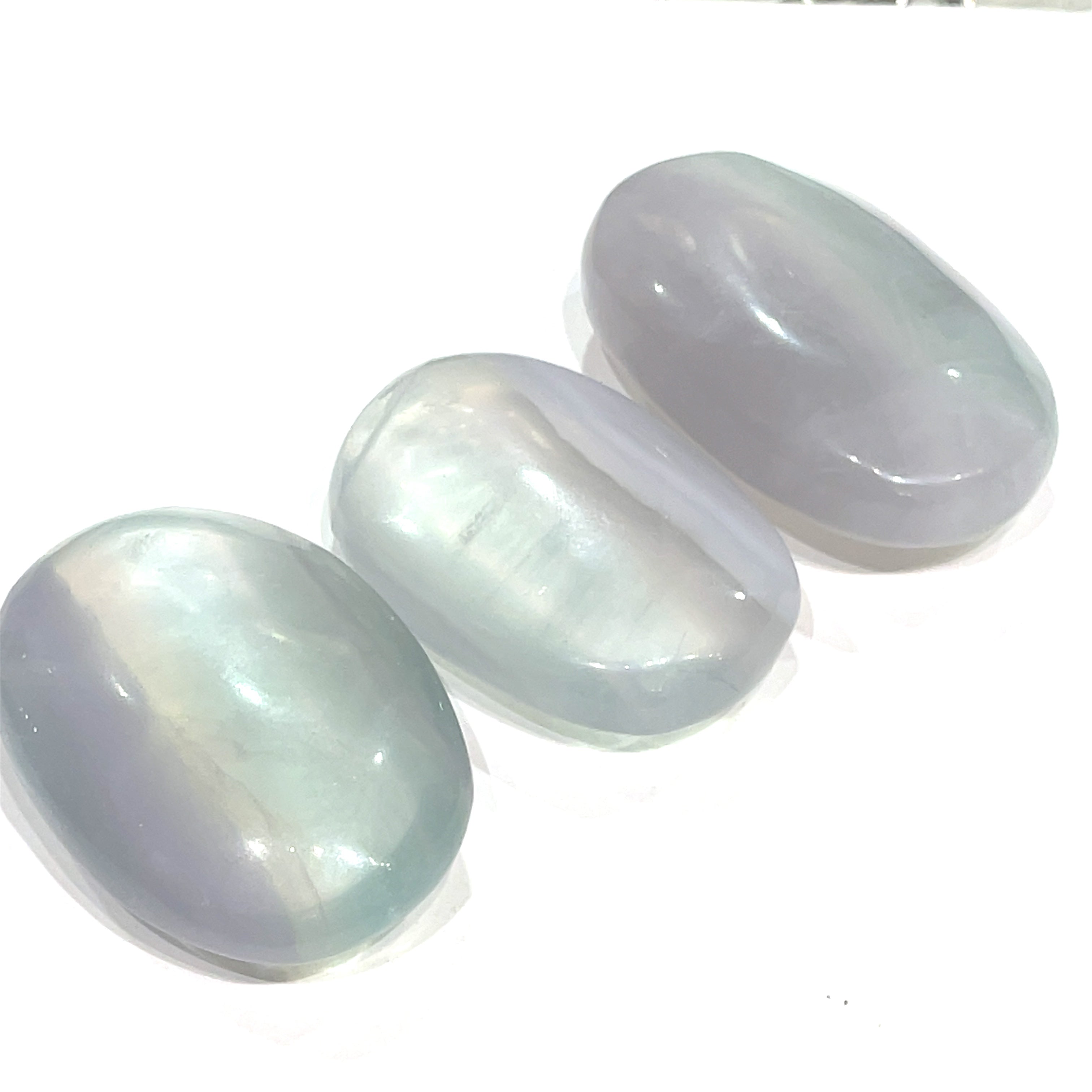 Another grouping of smooth, rounded gemstone palm stones displaying varying shades of lavender and green, with a milky translucency on a white background close up  overview.