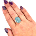 Aquamarine gemstone ring with a bezel-set design, worn on a model's finger, with a matching nail polish in the background front overview.