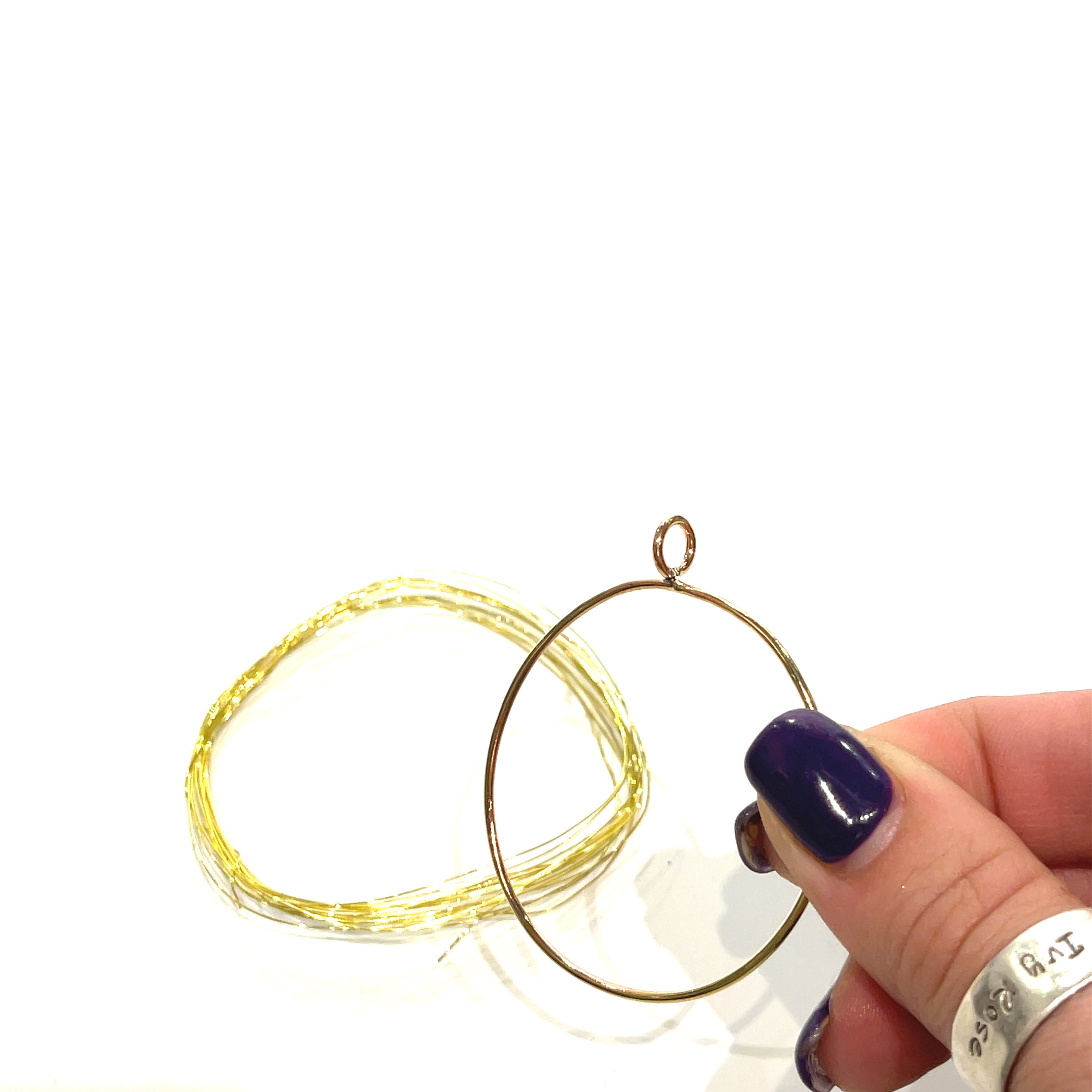 Brass Wire and the pendant outline in a model's hand on a white background, front view. 