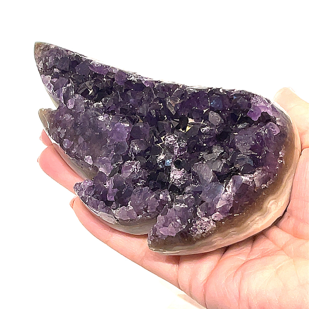 Carved amethyst gemstone in the shape of a butterfly wing with a purple color front view on a white background on a models hand.