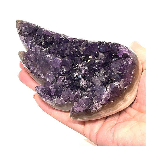 Carved amethyst gemstone in the shape of a butterfly wing with a purple color front view on a white background on a models hand.
