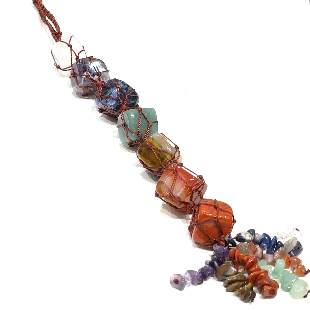 Chakra gemstone wall hanging with seven tumbled stones and gemstone tassel on a white background long diagonal overview. 