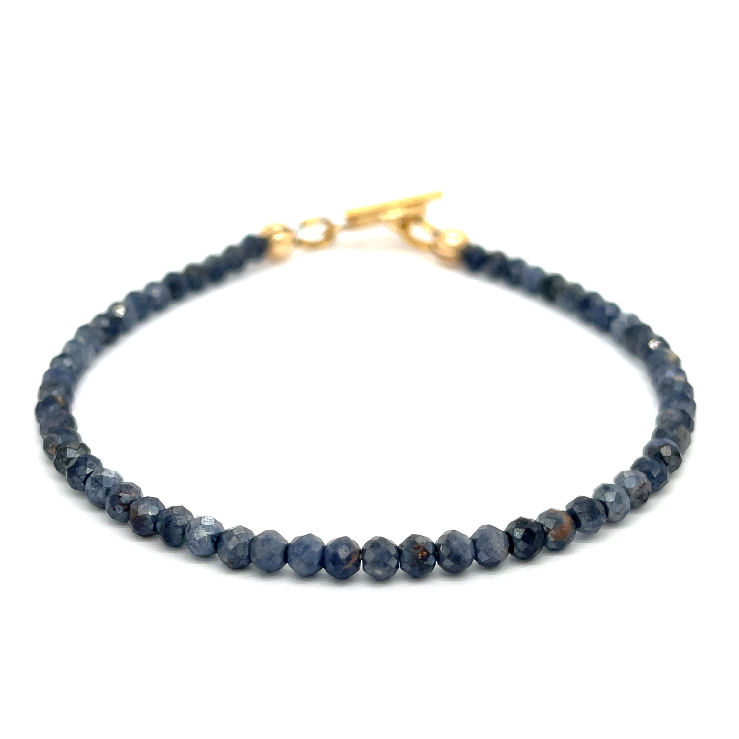 Close-up of 3mm faceted blue sapphires strung on steel cord showing vivid color and sparkle on a white background front overview.