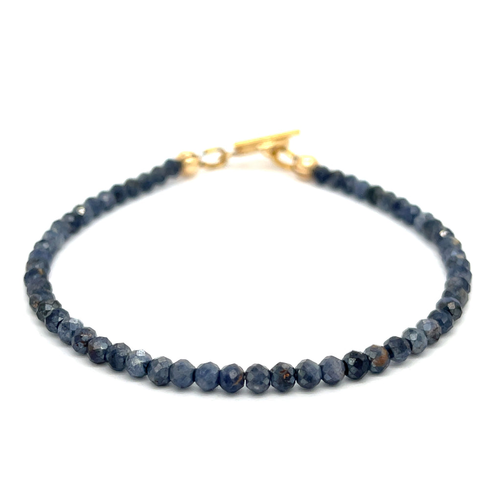 Close-up of 3mm faceted blue sapphires strung on steel cord showing vivid color and sparkle on a white background front overview.