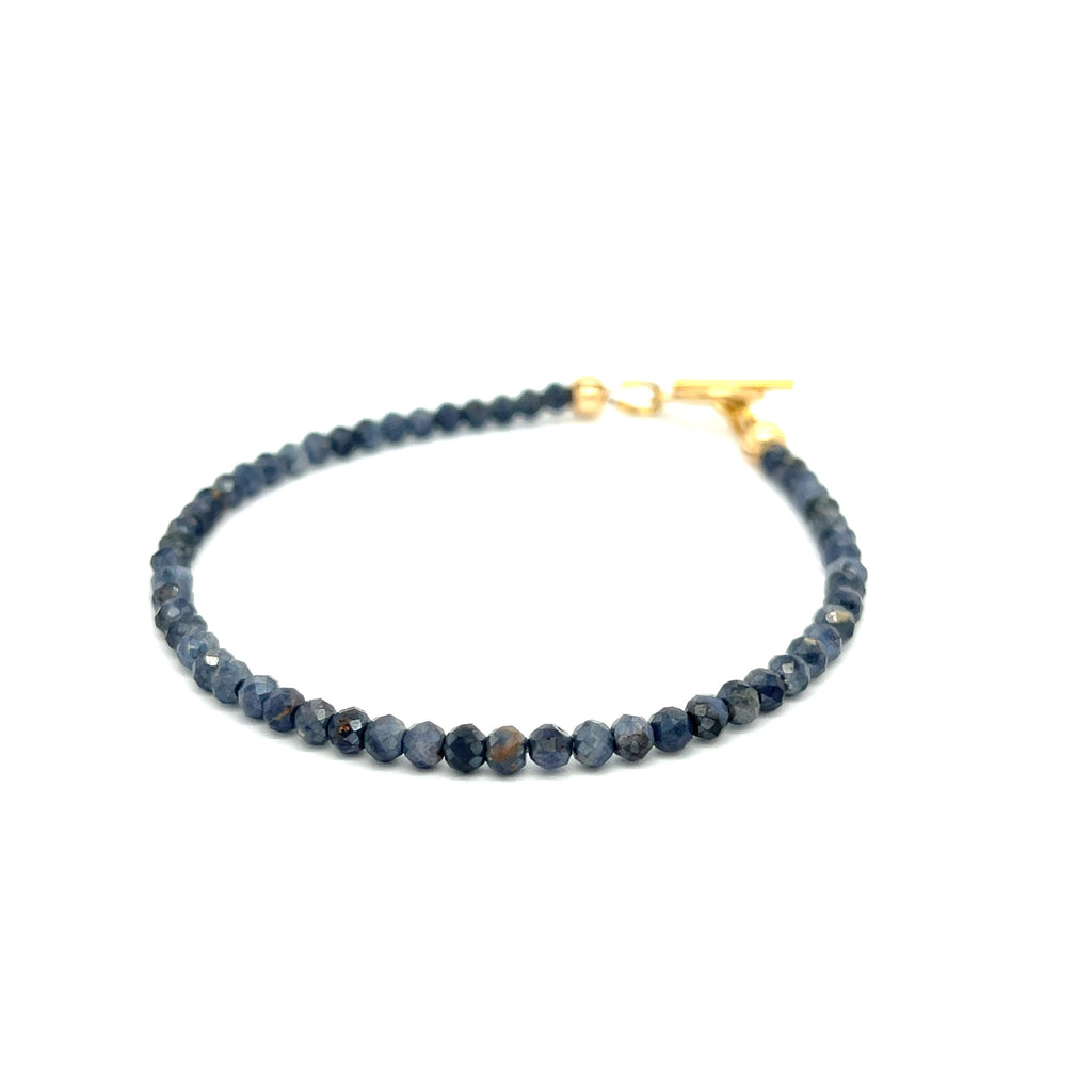 Close-up of 3mm faceted blue sapphires strung on steel cord showing vivid color and sparkle on a white background slight left angle overview.