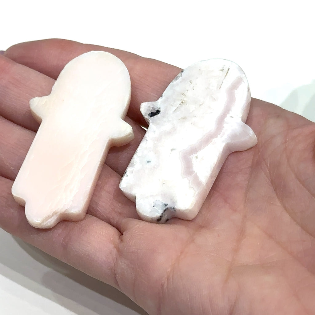 Close-up of Peruvian Pink Opal Hamsa showing natural color variations in models hand on white background front view.
