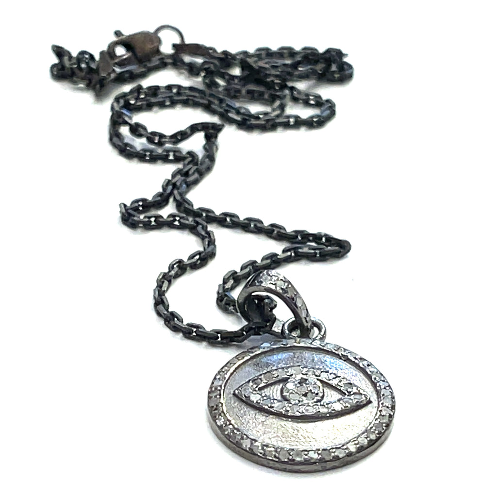 Close-up of diamond pavé Evil Eye pendant showing oxidized texture and detail on a white background flat center long overview.