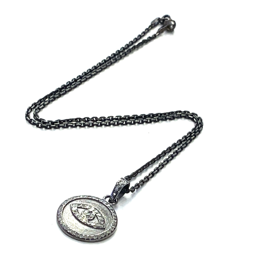 Close-up of diamond pavé Evil Eye pendant showing oxidized texture and detail on a white background flat center long zig zag overview.