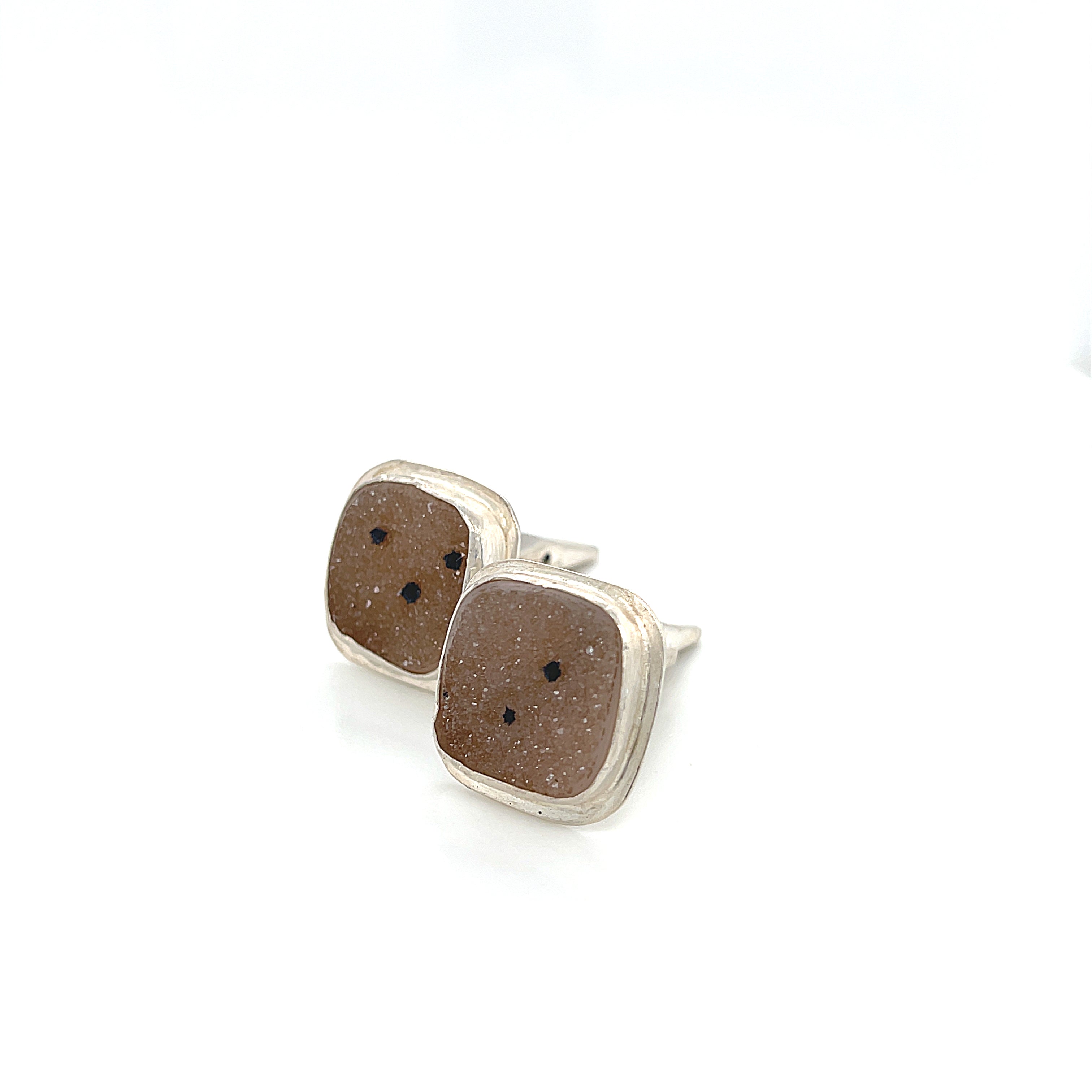 Close-up of natural quartz crystal, druzy texture, with brown inclusions, gemstone, with sterling silver cufflinks on a white background, front left angle close up overview.