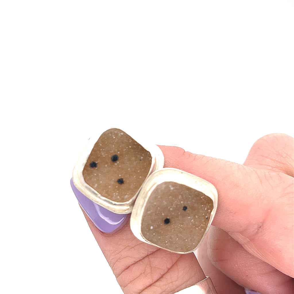 Close-up of natural quartz crystal druzy texture with brown inclusions gemstone with sterling silver cufflinks on a white background in models fingertips overview.