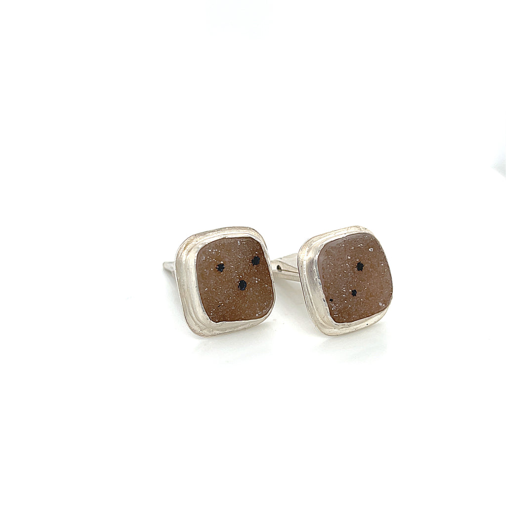 Close-up of natural quartz crystal, druzy texture, with brown inclusions, gemstone, with sterling silver cufflinks on a white background, slight right-angle overview.