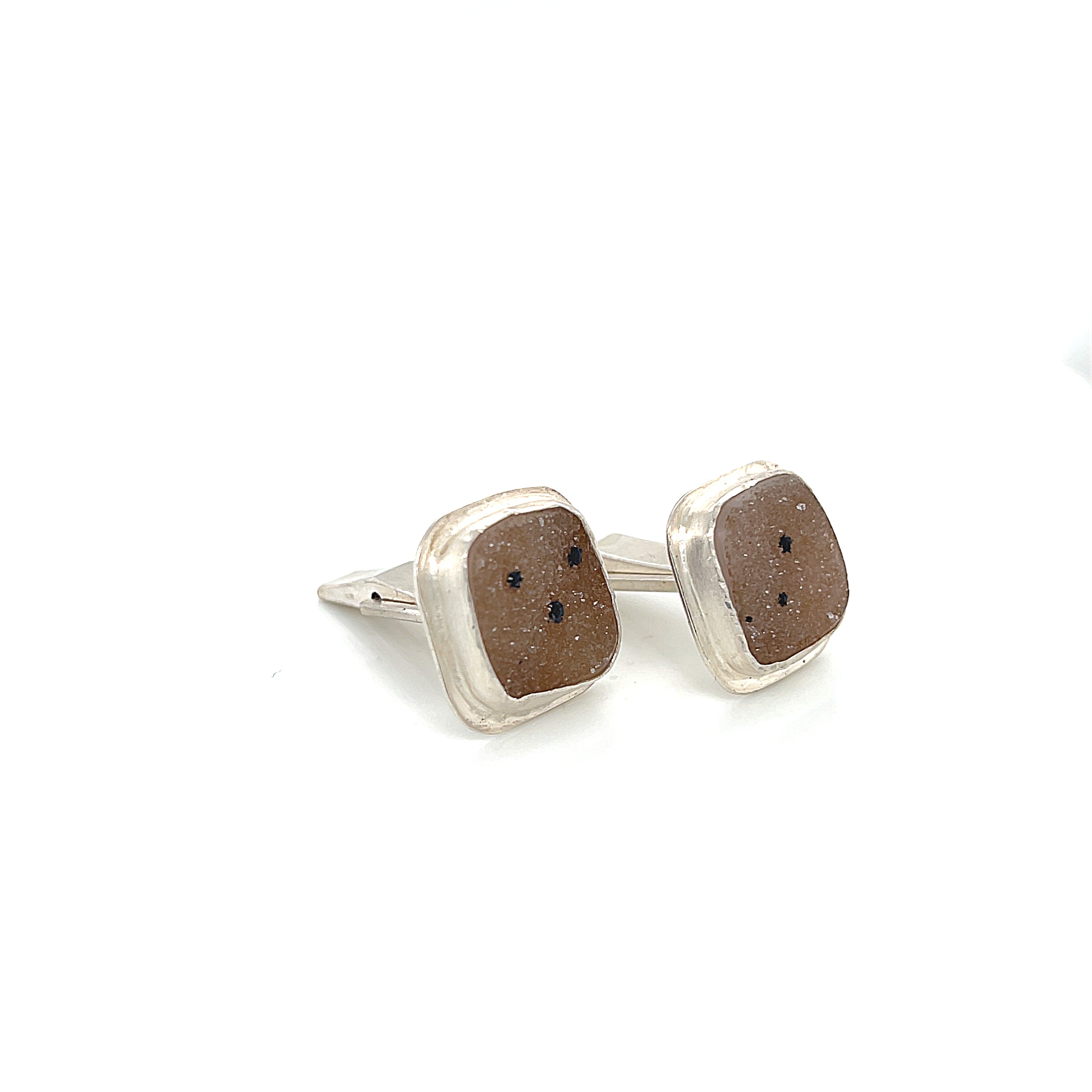 Close-up of natural quartz crystal druzy texture with brown inclusions gemstone with sterling silver cufflinks on a white background slight right angle overview.