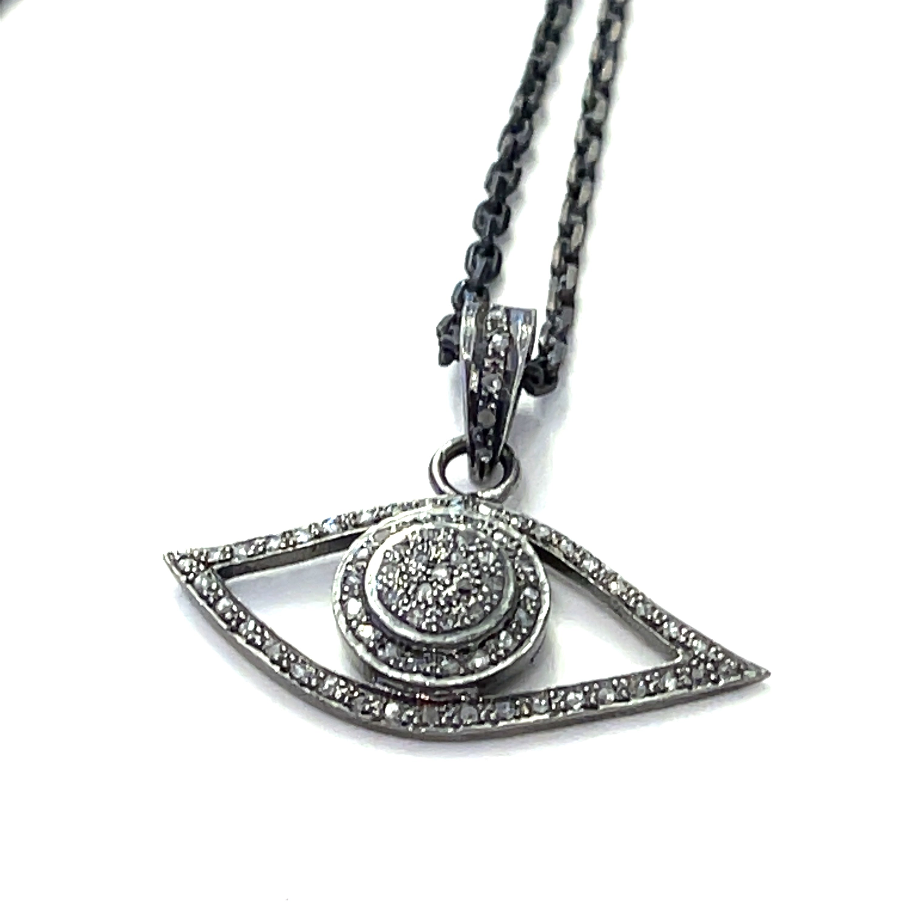 Close-up of pavé diamond Evil Eye pendant showing oxidized texture and sparkle on a white background center long hanging overview.