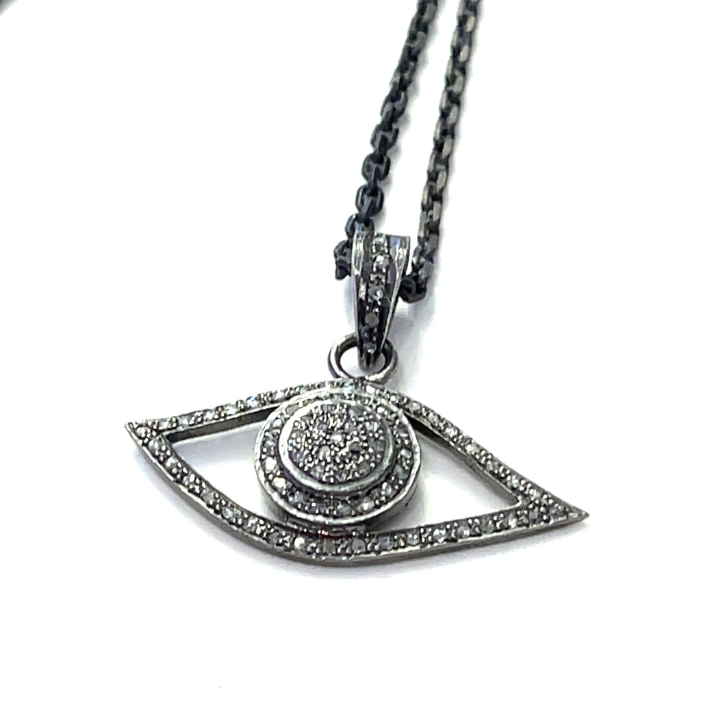Close-up of pavé diamond Evil Eye pendant showing oxidized texture and sparkle on a white background center long hanging overview.