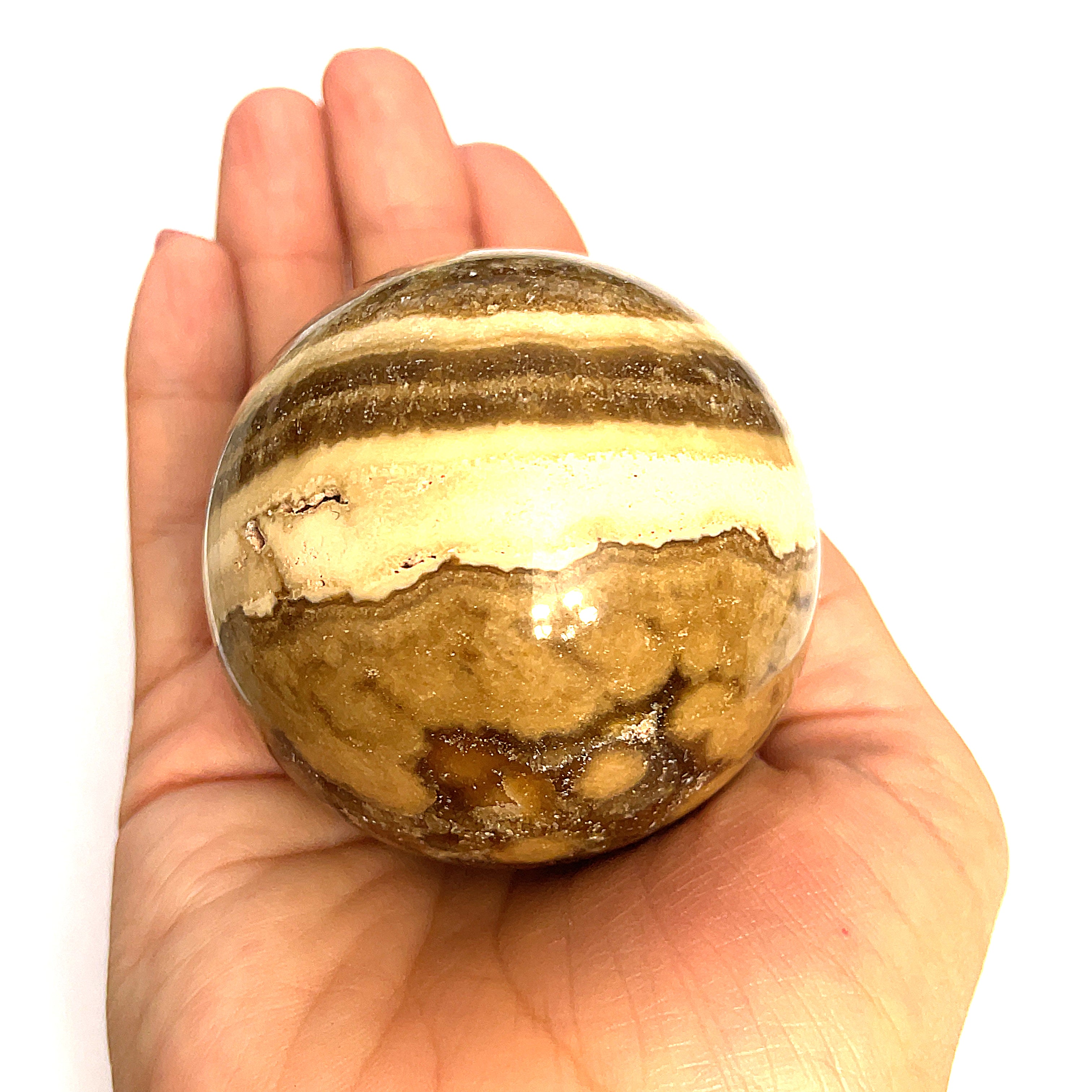 Close-up of polished Chocolate Calcite sphere on a models hand for a close up, front, overview.