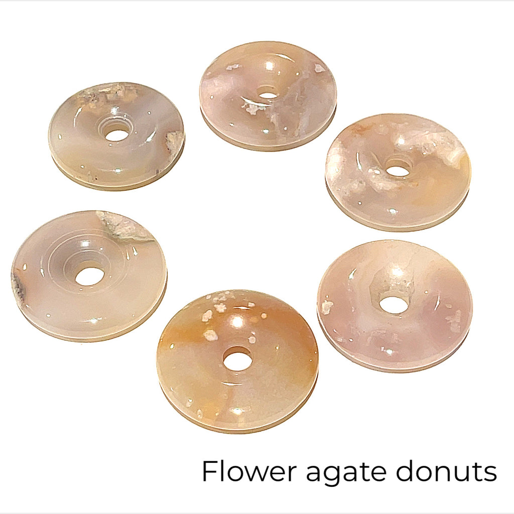 Close-up of polished gemstone donuts showing natural color and pattern variations on several Flower Agate front overview on white background