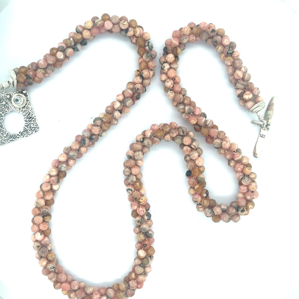 Hand-crocheted Rhodochrosite gemstone necklace with sterling silver toggle and Blue Topaz accent – Hidden Jewel of the South End on a white background, a long center close up overview. 