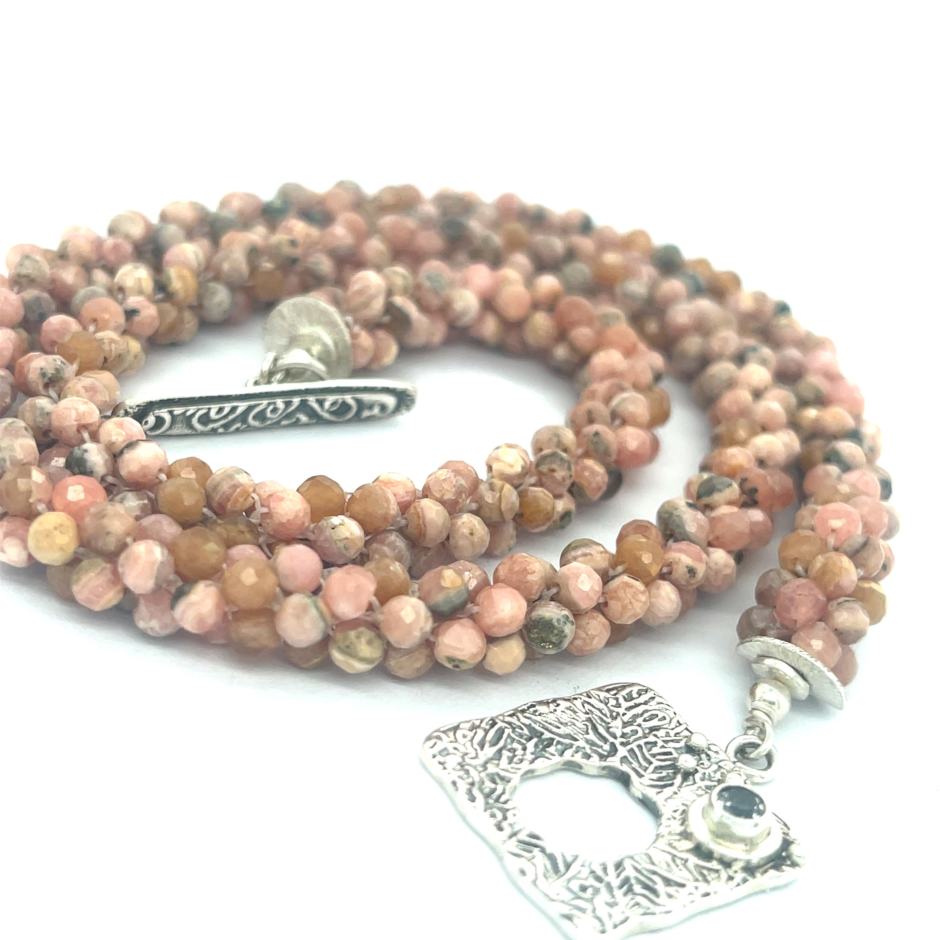 Hand-crocheted Rhodochrosite gemstone necklace with sterling silver toggle and Blue Topaz accent – Hidden Jewel of the South End on a white background, a spiral close up overview.