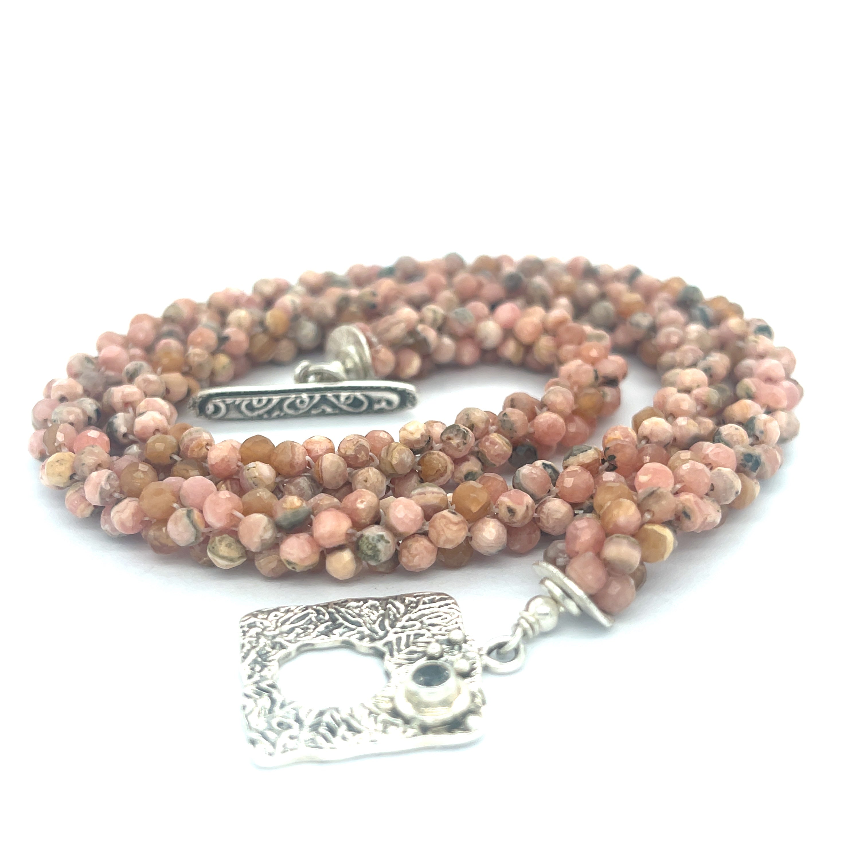 Hand-crocheted Rhodochrosite gemstone necklace with sterling silver toggle and Blue Topaz accent toggle  on a white background, a spiral center close up overview. 