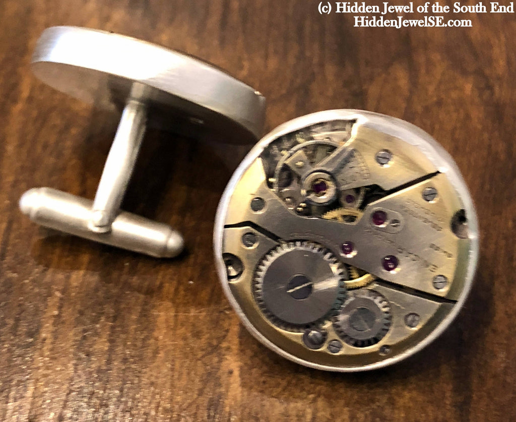 Handcrafted antique watch movement cuff links in sterling silver on a wood background close up front and back overview.
