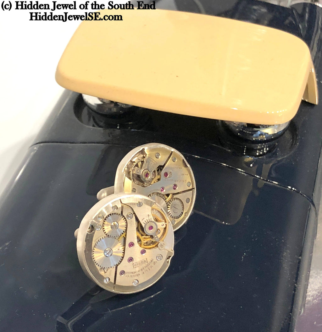 Handcrafted antique watch movement cuff links in sterling silver on a wood background close up front slight right angle overview.