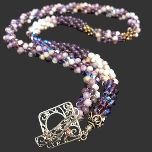 A crocheted necklace made with amethyst rounds and Swarovski crystal bicone beads in purple and white colors, featuring a sterling silver toggle clasp.
