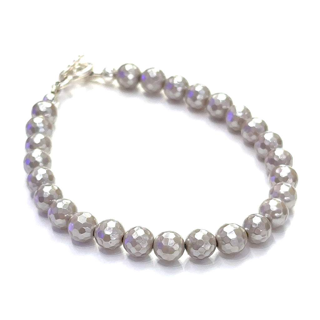 Mother of Pearl gemstone bracelet with faceted 6mm beads and sterling silver hammered toggle clasp handmade by Hidden Jewel. on a white background slight right angle overview.