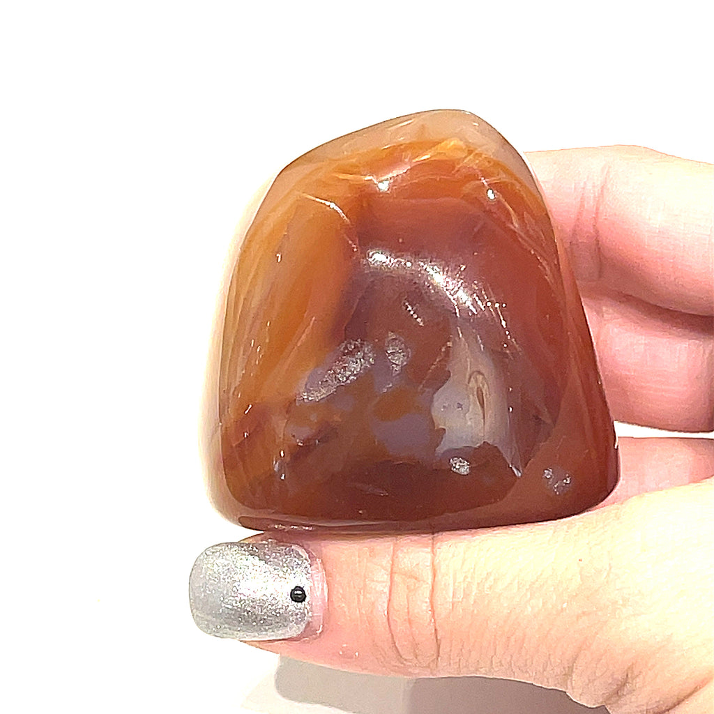 One Carnelian gemstones free-form shapes displayed in a models hand on a white background, front view. 